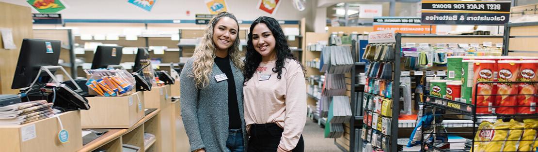 Two Student workers stand smiling in a Pima Bookstore